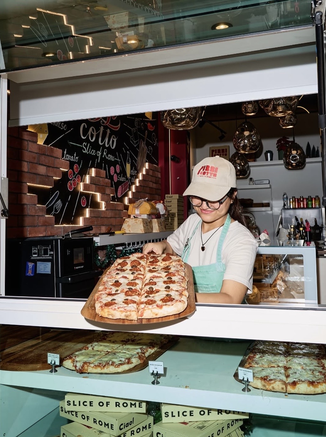 Pizzicotto staff member holding a sliced pizza at the display case